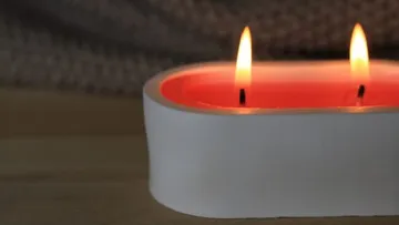 Zwei Kerzen brennen in einem weißen Behälter.