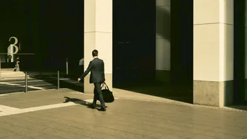 Man in suit walks through urban environment with bag.