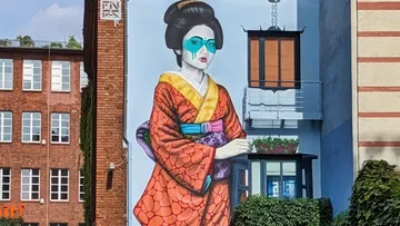 Wandgemälde einer Geisha mit buntem Kleid an einem Gebäude.