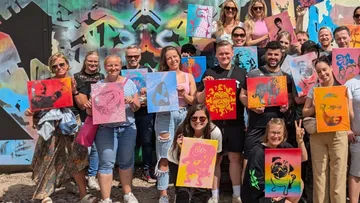 Group of people holding colorful works of art in front of a wall.