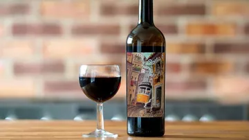 Weinflasche und Glas, Rotwein steht auf Holztisch.