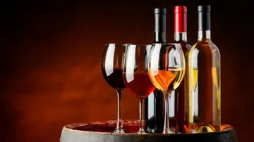 The wine bottle and glasses are placed on a barrel in the dark.