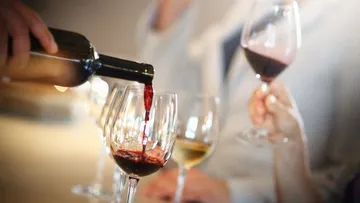 Wein wird aus einer Flasche in Gläser gegossen.