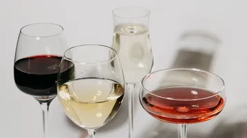 Vier Weingläser mit verschiedenen Getränken auf einem Tisch.