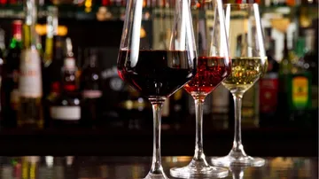 Drei Weingläser stehen auf einer Bar mit Alkoholflaschen.