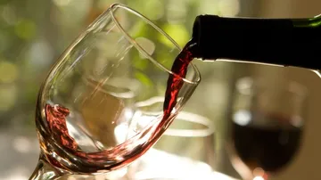 Weinglas wird mit Rotwein gefüllt, Umgebungslicht ist weich.