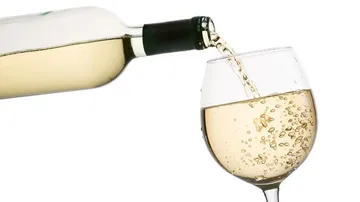A wine bottle pours white wine into a glass.