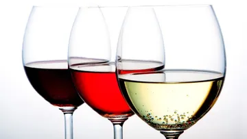 Three wine glasses with red, rosé and white wine stand side by side.