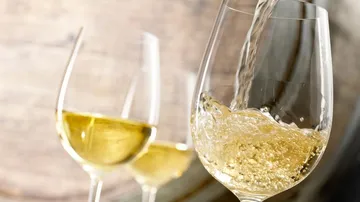 Weißwein wird in ein Glas gegossen, Hintergrund mit Holzfass.