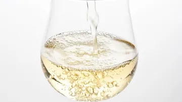 Weißwein wird sprudelnd in ein Glas gegossen.