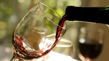 Ein Weinglas wird mit rotem Wein gefüllt. Helles Licht.