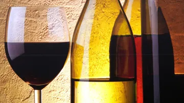 A wine glass stands next to several bottles.