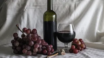 Wine bottle with glass and grapes on a table.