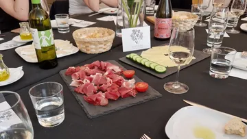 Platte mit Wurst, Gemüse, Getränken auf Tisch gedeckt.