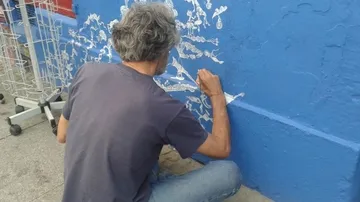 Ein Mann malt mit weißer Farbe auf blauer Wand.