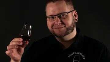 Man holding glass, smiling against a dark background.