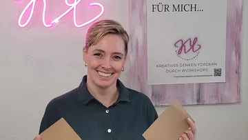Frau hält zwei Karten in einem kreativen Workshop-Raum.