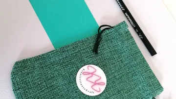 Grüne Tasche liegt mit einem Stift auf einem Tisch.