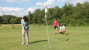 Eine Golferin puttet auf dem Grün, Zuschauer beobachten aufmerksam.