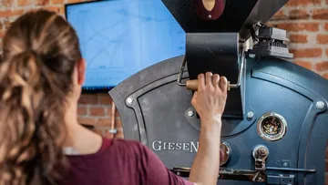 Eine Person betätigt eine Kaffeemaschine in einer Rösterei.