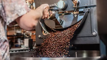 Kaffeebohnen werden aus einer Maschine in einen Behälter geleitet.
