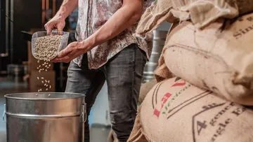 Ein Mann schüttet Kaffeebohnen in einen Metallbehälter.
