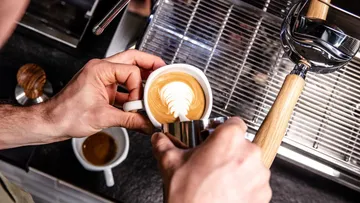Kaffee in Tasse wird mit Milchschaum verziert. Küchenumgebung.