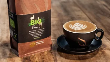 Kaffeetasse mit dekorativer Oberfläche neben Kaffeesack auf Holz.