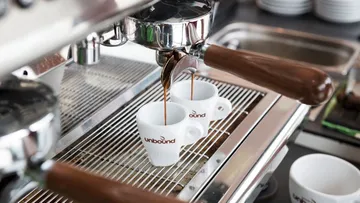 Zwei Tassen fangen Espresso aus einer Kaffeemaschine auf.