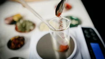 A spoon adds spice to a mug on a scale.