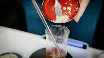 A hand pours powder into a beaker.