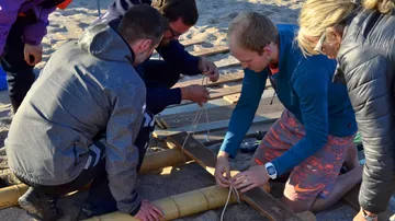 People build a structure together using wood and ropes.