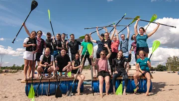Group of people posing on a homemade raft on the beach.