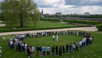 Gruppierung von Menschen bildet einen Kreis auf Rasenfläche.
