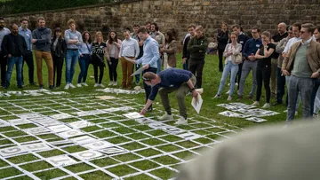 Menschen beobachten; Teilnehmer platzieren Buchstaben auf Grasfläche.
