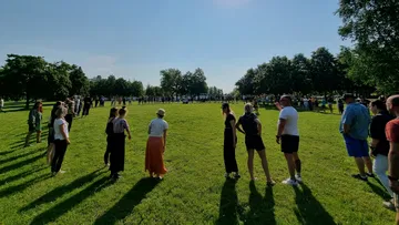 Gruppierte Menschen stehen auf einer Wiese bei Sonnenschein.