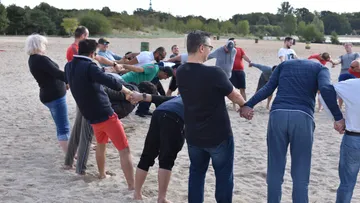Gruppen Menschen halten sich an den Händen am Strand.