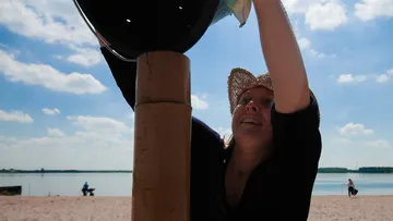 Woman wearing a hat grabs something on the beach when the sky is clear.