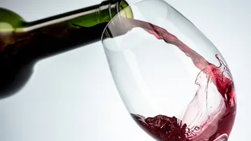 Eine Weinflasche gießt roten Wein in ein Glas.