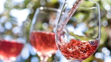 Rosenwein wird in Gläser gegossen, umgeben von Pflanzen.