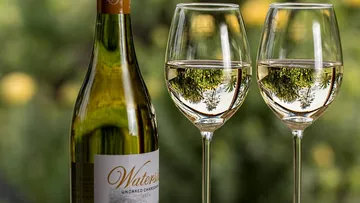 Wine bottle stands next to two glasses of white wine.