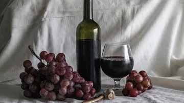 Wine bottle and glass with red grapes on table.
