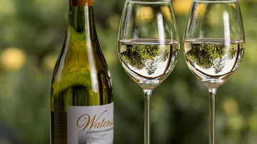 Flasche Wein neben zwei Gläsern mit reflektierendem Inhalt.