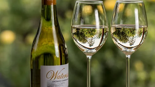 Wine bottle next to two glasses of Chardonnay, blurred surroundings.