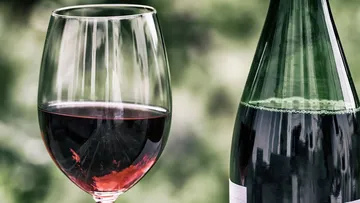 Weinglas mit Rotwein steht neben einer Flasche Wein.