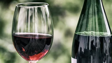 Ein Weinglas steht neben einer Flasche Wein.