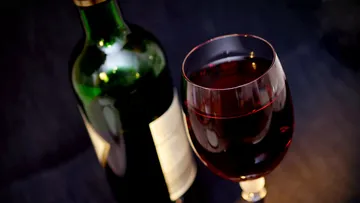 Wine bottle next to a filled wine glass on a black table.