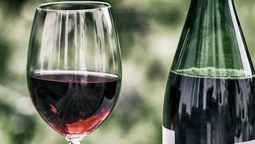 Ein Glas mit Rotwein steht neben einer Flasche.