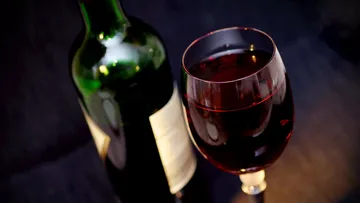 Wine bottle next to a fully filled red wine glass on a table.