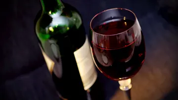 Weinglas mit Rotwein steht neben einer Flasche.